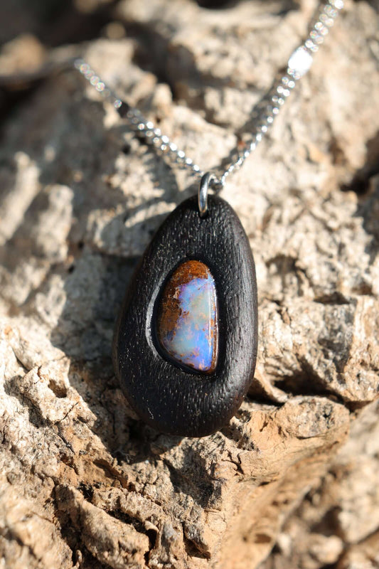 Holzkette - Boulder Opal in dunklem Edelholz mit elegantem Design aus Edelstahl auf natürlichem Untergrund.