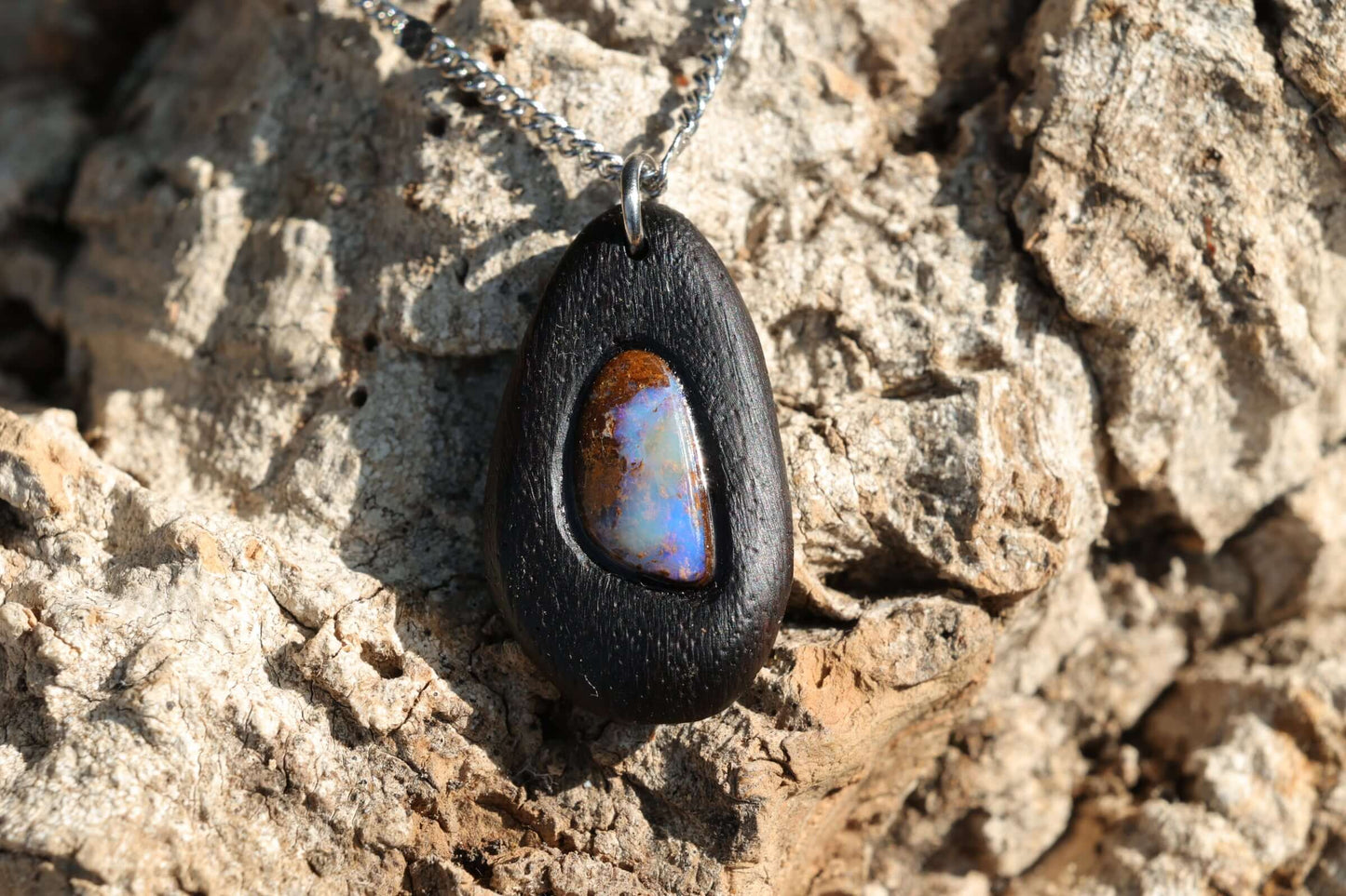 Holzkette - Boulder Opal in dunklem Edelholz, modern und elegant, aus Edelstahl gefertigt, vor natürlichem Hintergrund.